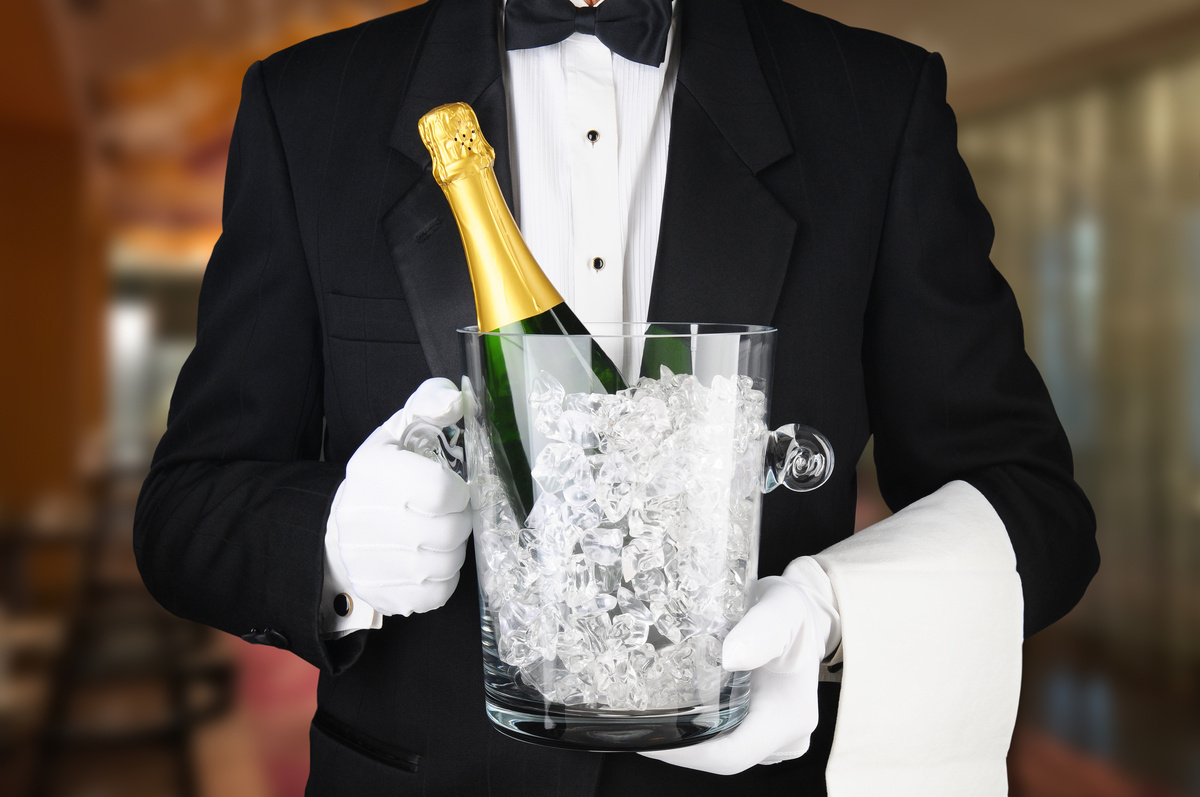 A waiter in a restaurant carrying an ice bucket with a bottle of unopened champagne glaçons